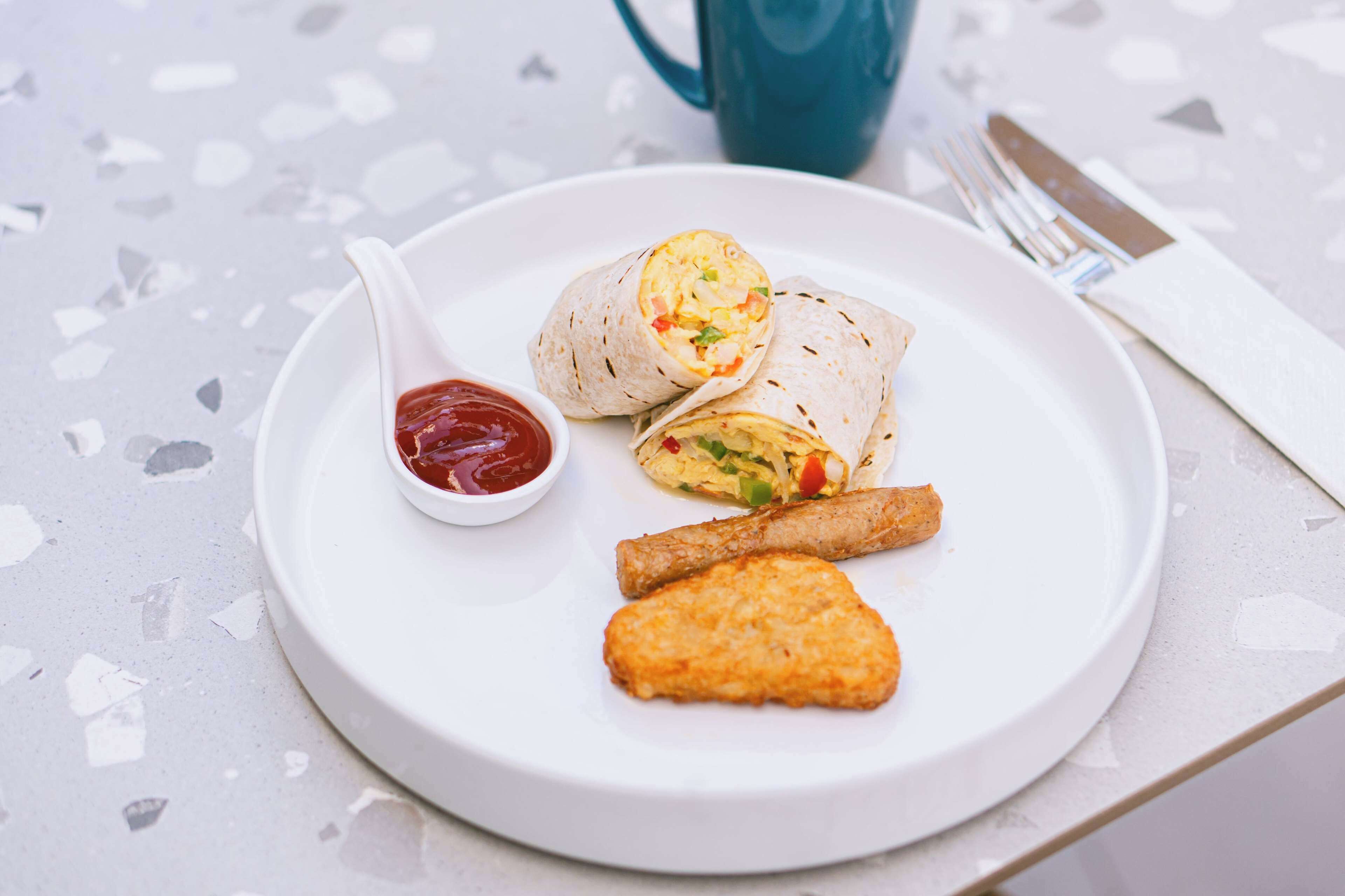 Un plato con un burrito, un pedazo de pollo frito y un recipiente pequeño de kétchup.