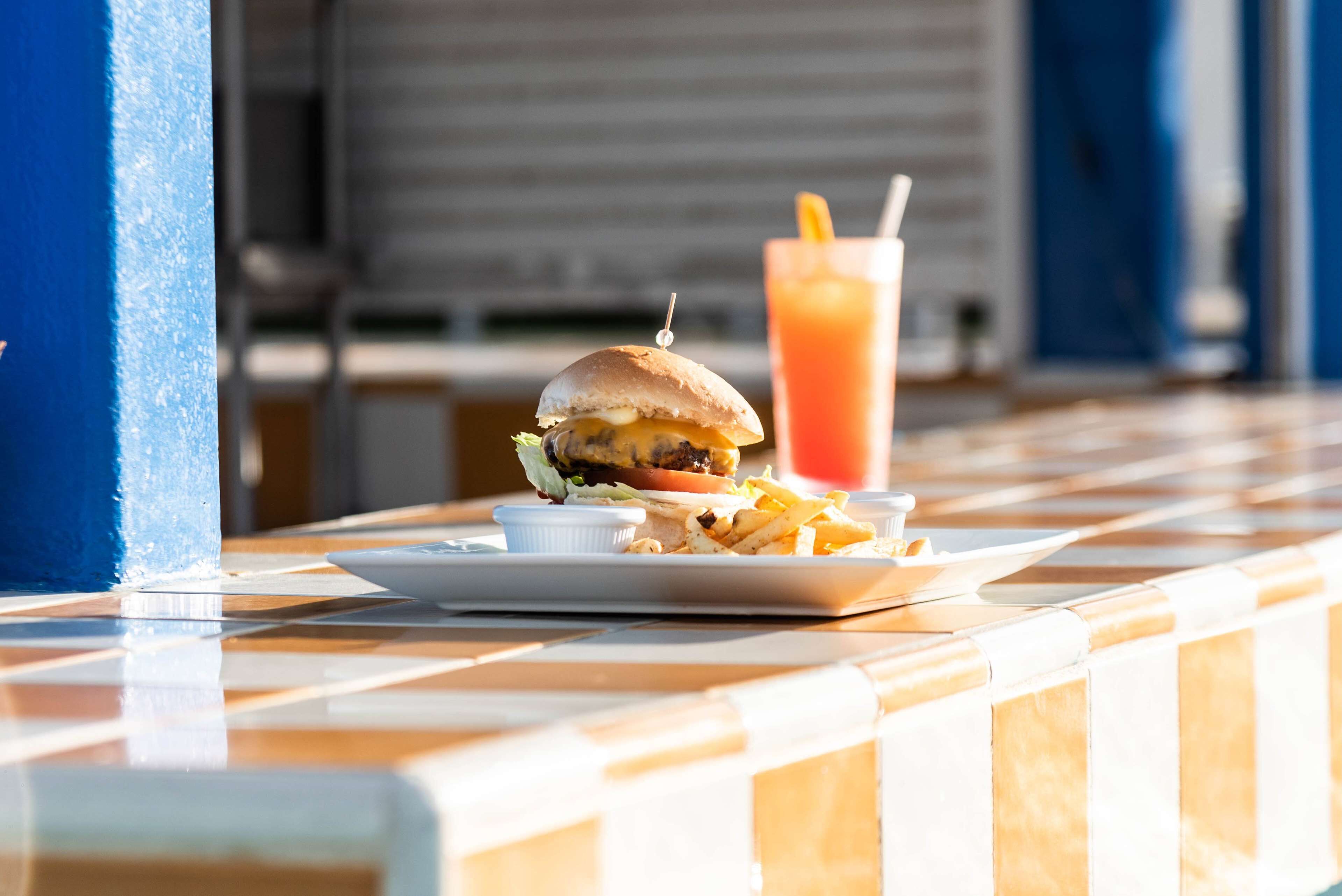 A burger and fries on a table with a drink in the background.
