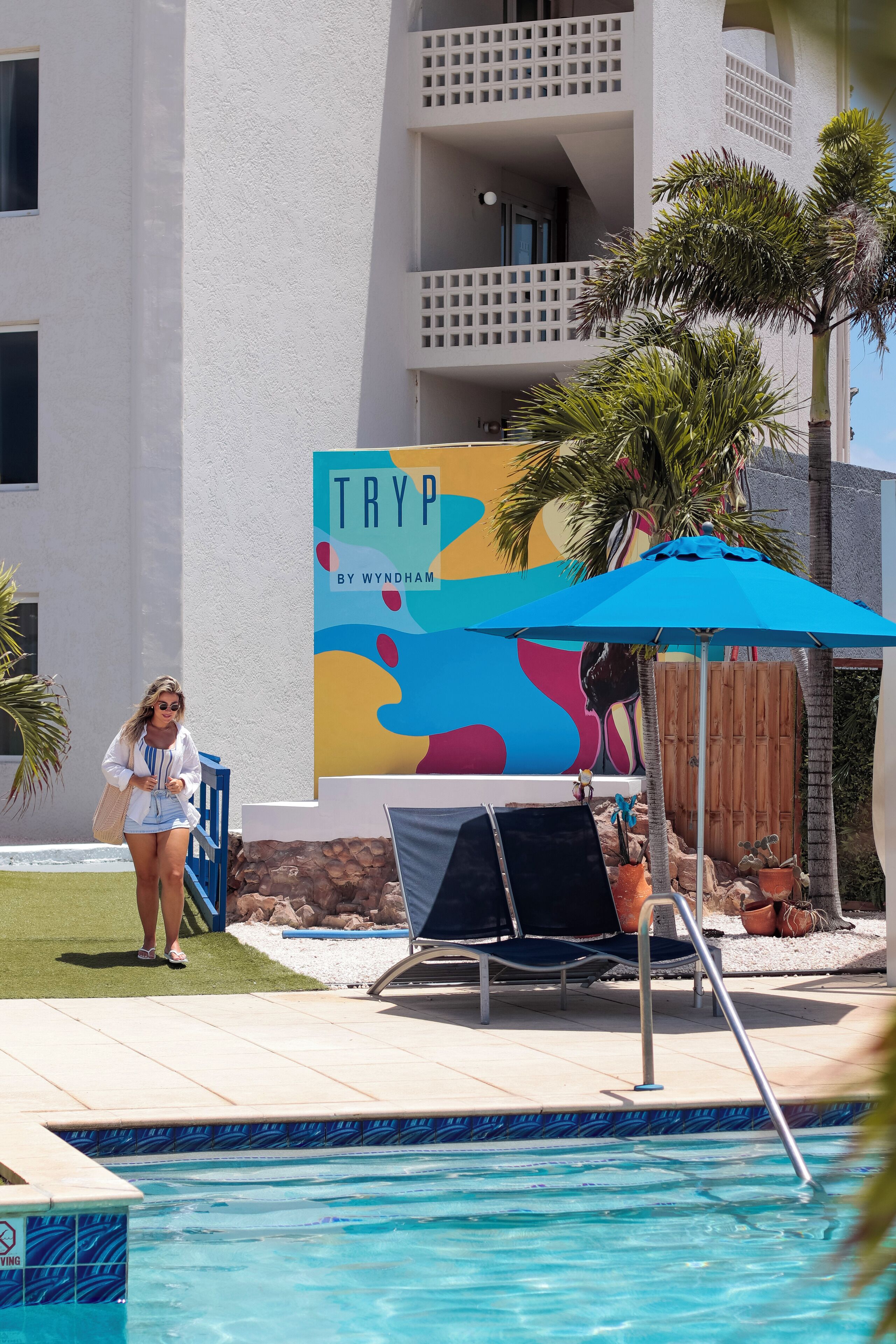 Un espace piscine avec des chaises longues, un panneau indiquant « TRYP BY WYNDHAM », et un bâtiment doté de balcons.
