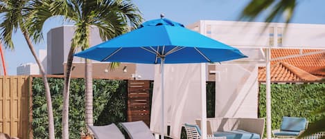 A poolside area with lounge chairs, a blue umbrella, and palm trees.