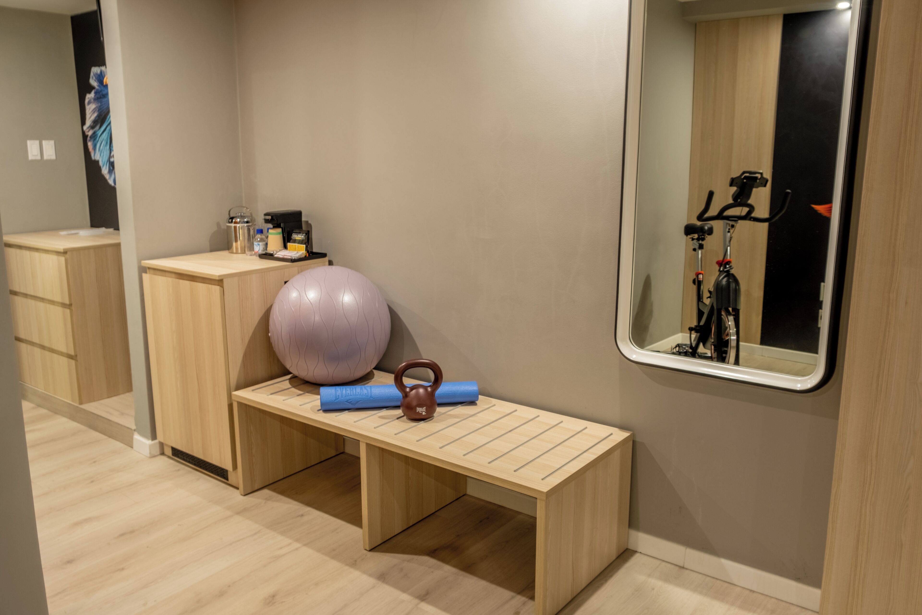 Ein Zimmer mit einer Holzbank, einer Kettlebell, einer Yogamatte und einer weiteren Kettlebell auf dem Boden.