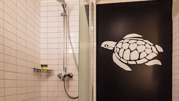 Un baño con ducha revestida de azulejos blancos, inodoro blanco y pared negra decorada con un vinilo de tortuga blanca.