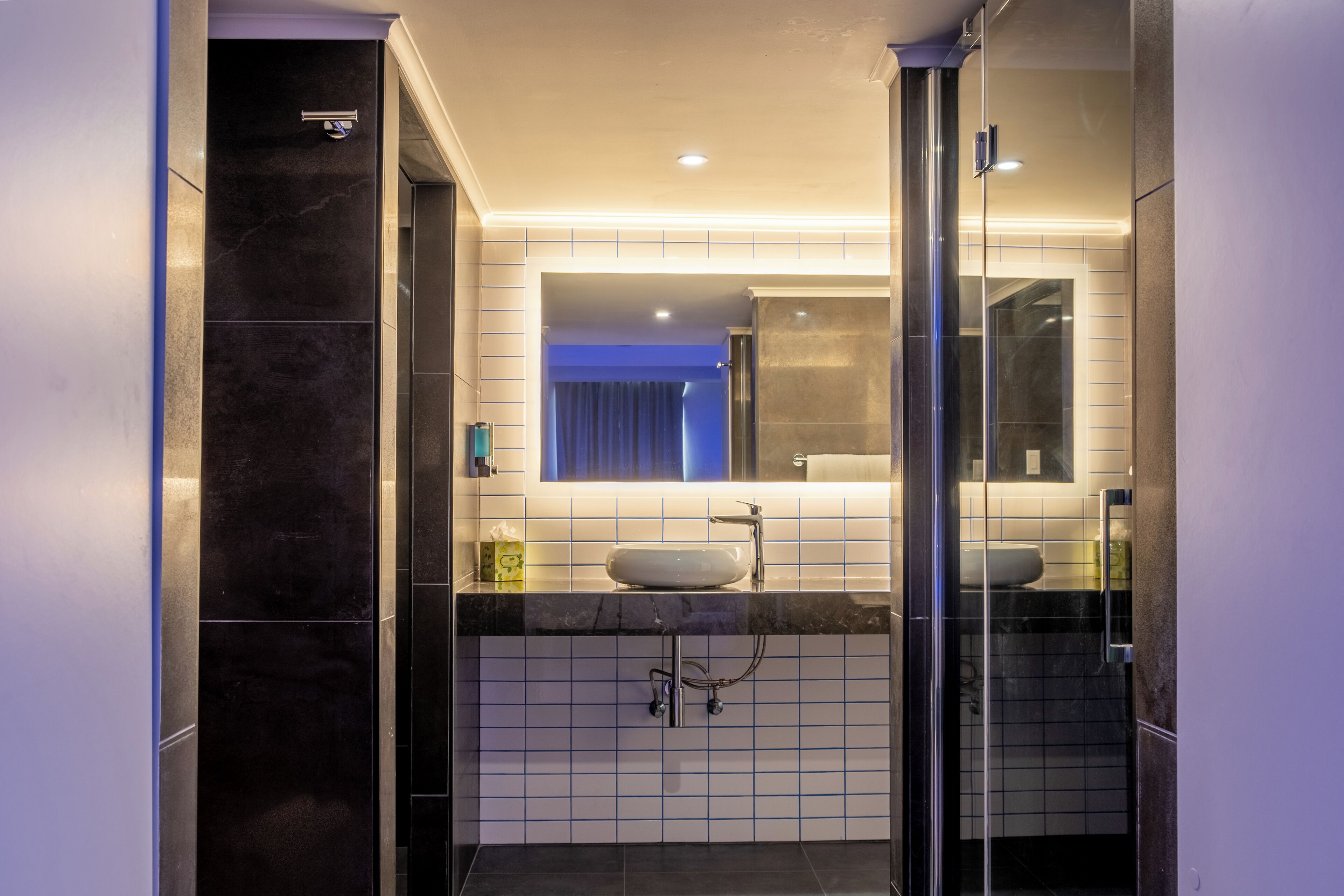 Une salle de bain moderne avec une douche à l’italienne en verre, un lavabo blanc et un grand miroir.