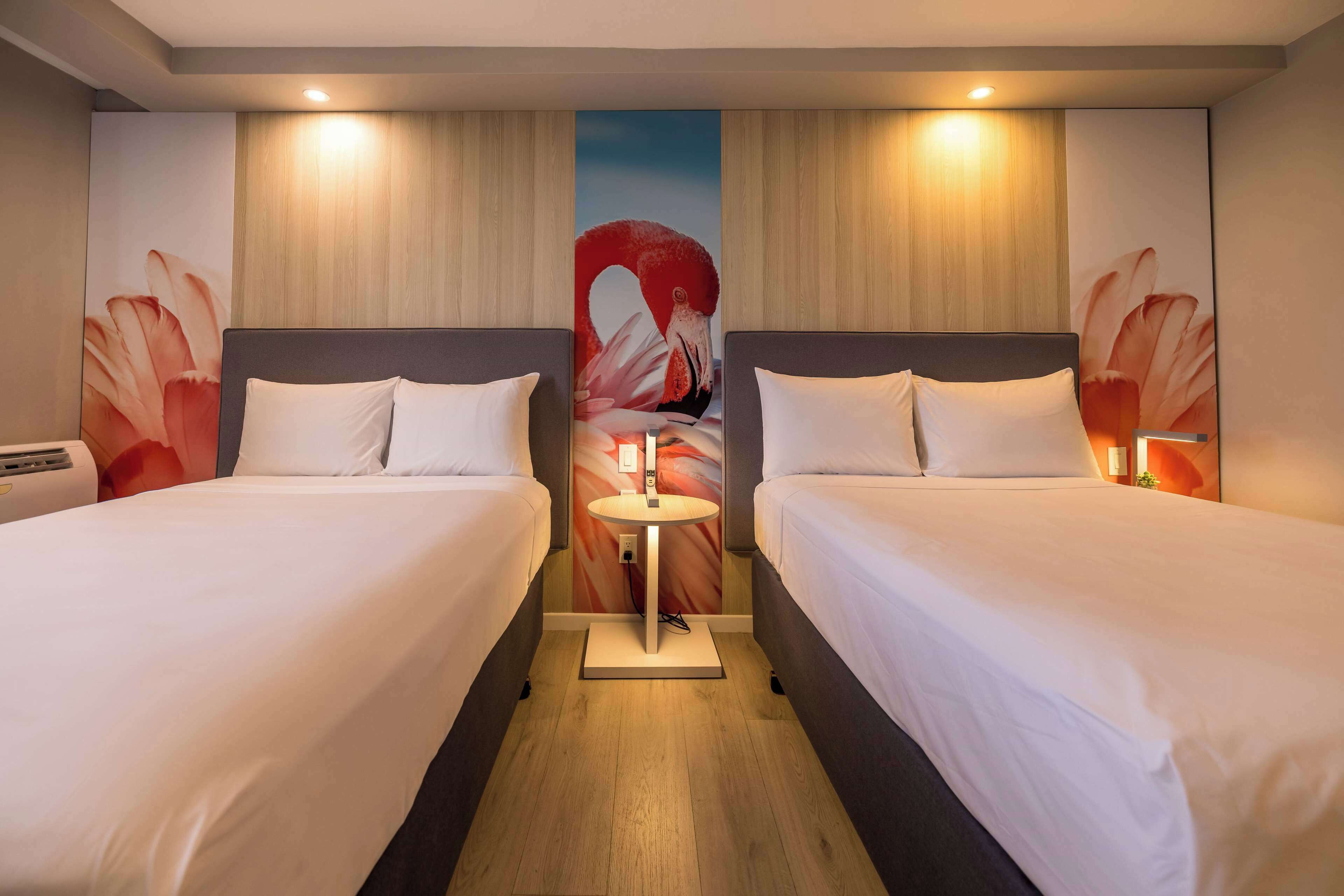 A hotel room with two beds, a central table, and a large wall mural.