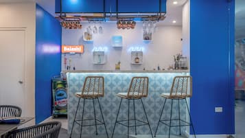 A bar area with three stools, a neon sign, and a counter with bottles and glasses.