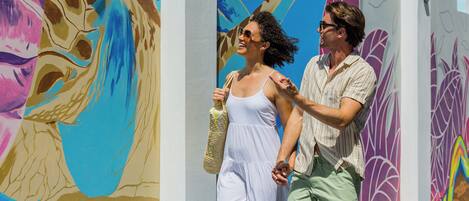 A couple walking past a colorful mural with abstract designs.