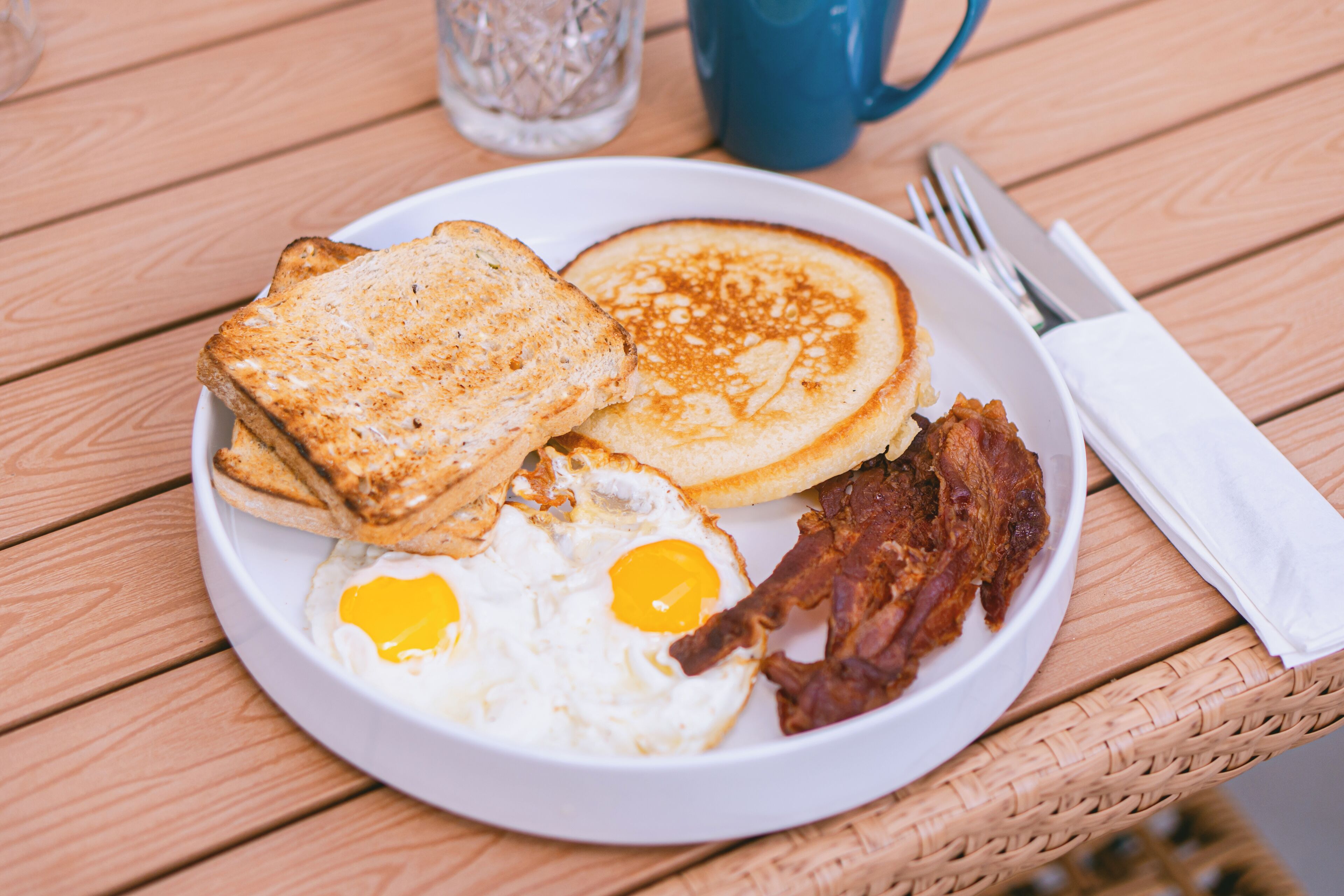 Un plato de desayuno con tostadas, panqueques, huevos fritos y tocino sobre una mesa de madera.