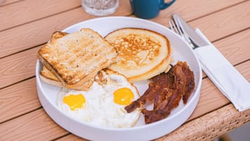 Un plato de desayuno con tostadas, panqueques, huevos fritos y tocino sobre una mesa de madera.