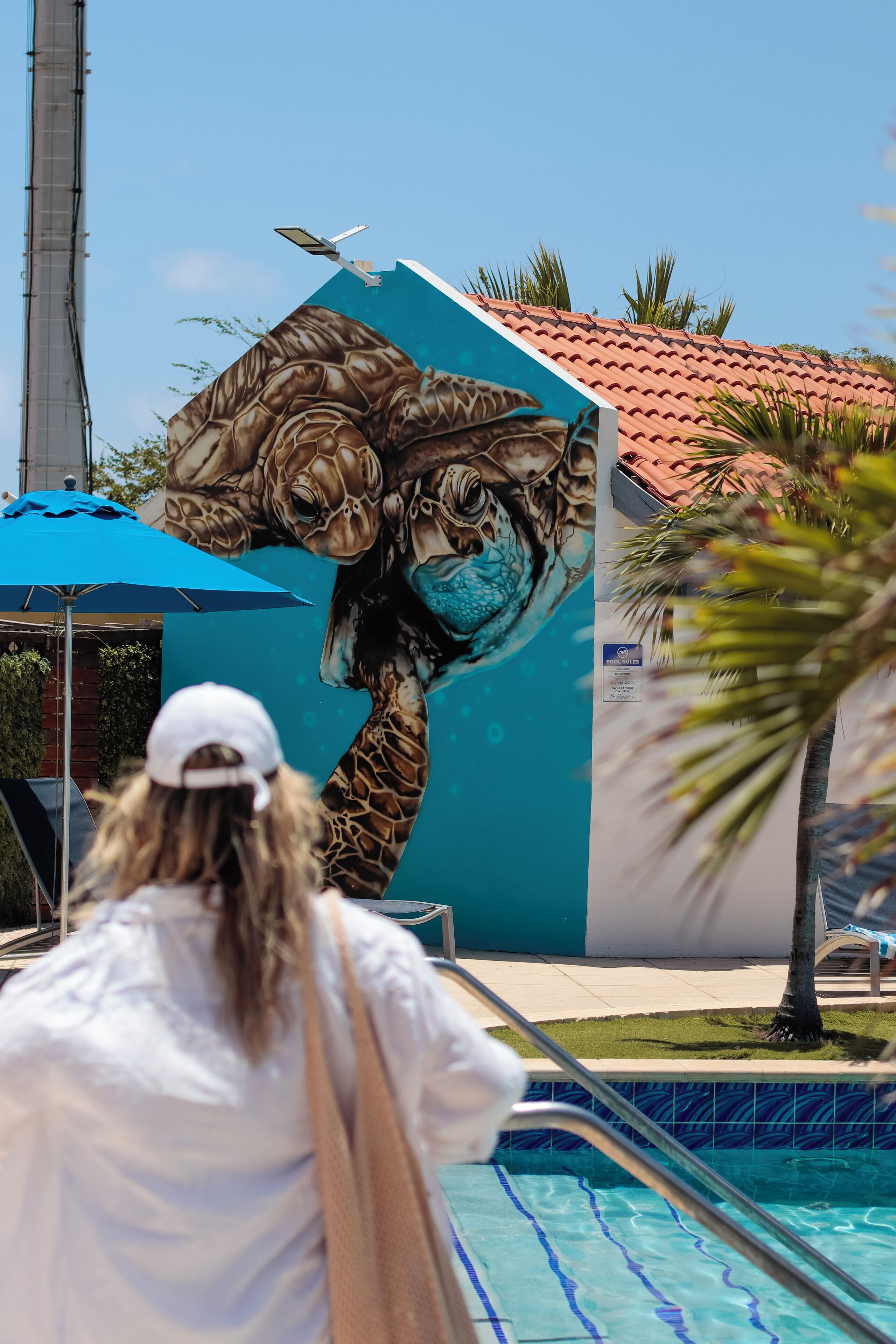 Una persona de pie junto a una piscina con un mural de la cabeza de una jirafa en la pared.