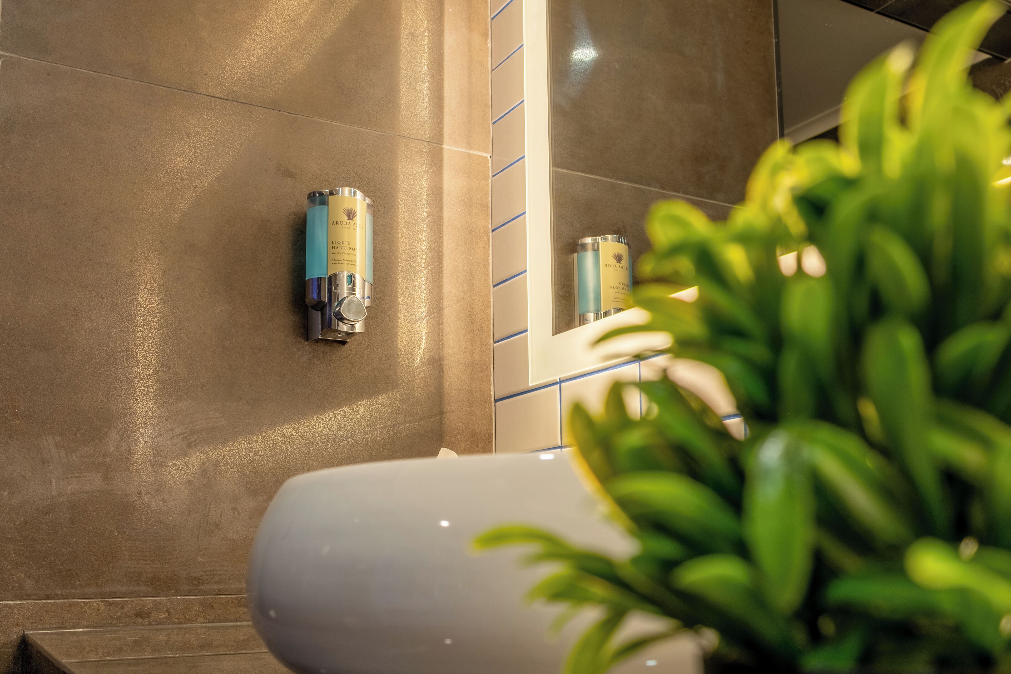 A bathroom with a large mirror, a white sink, and two bottles of hand sanitizer on the wall.