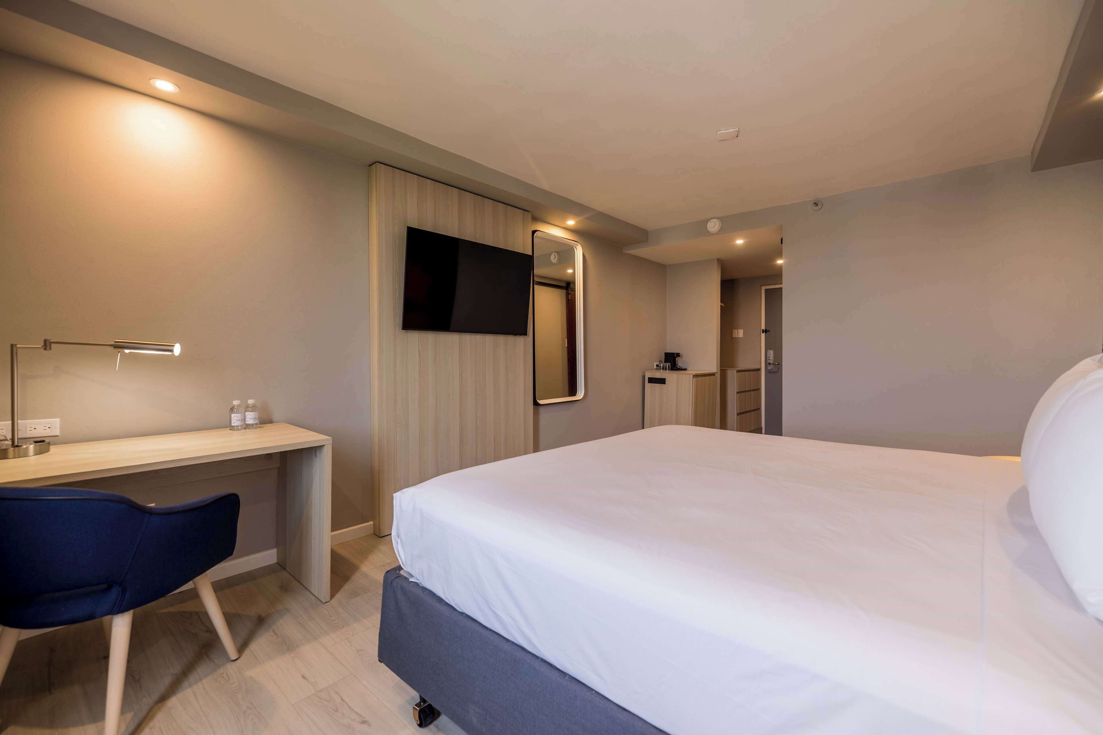 A modern hotel room with a bed, desk, chair, TV, and a mirror.