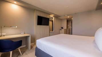 A modern hotel room with a bed, desk, chair, TV, and a mirror.