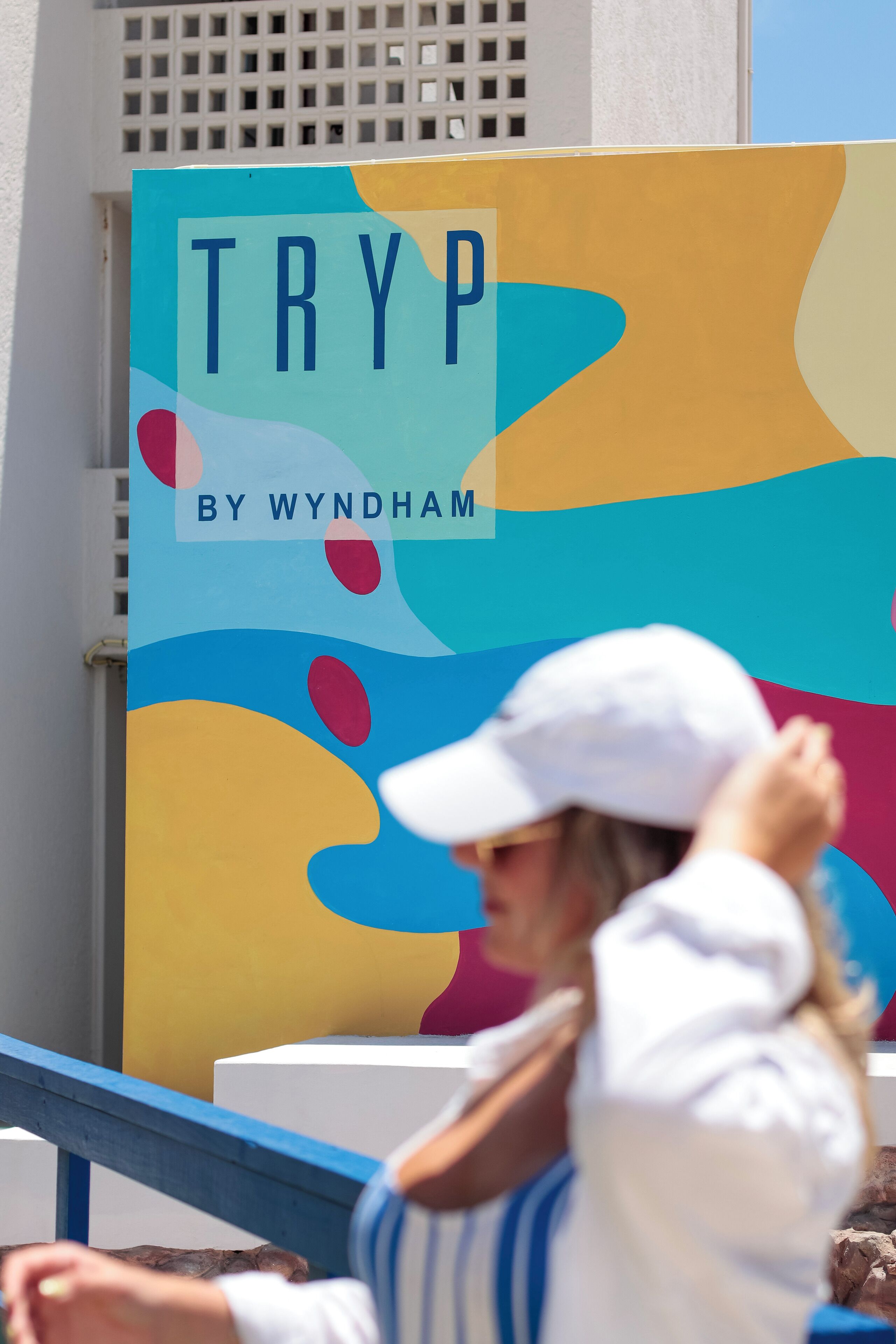 Een kleurrijk bord met de tekst 'TRYP BY WYNDHAM' voor een achtergrond van abstracte vormen.