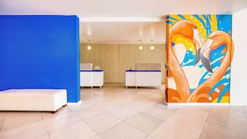 A reception area with a blue wall, a white bench, and a colorful painting of birds.