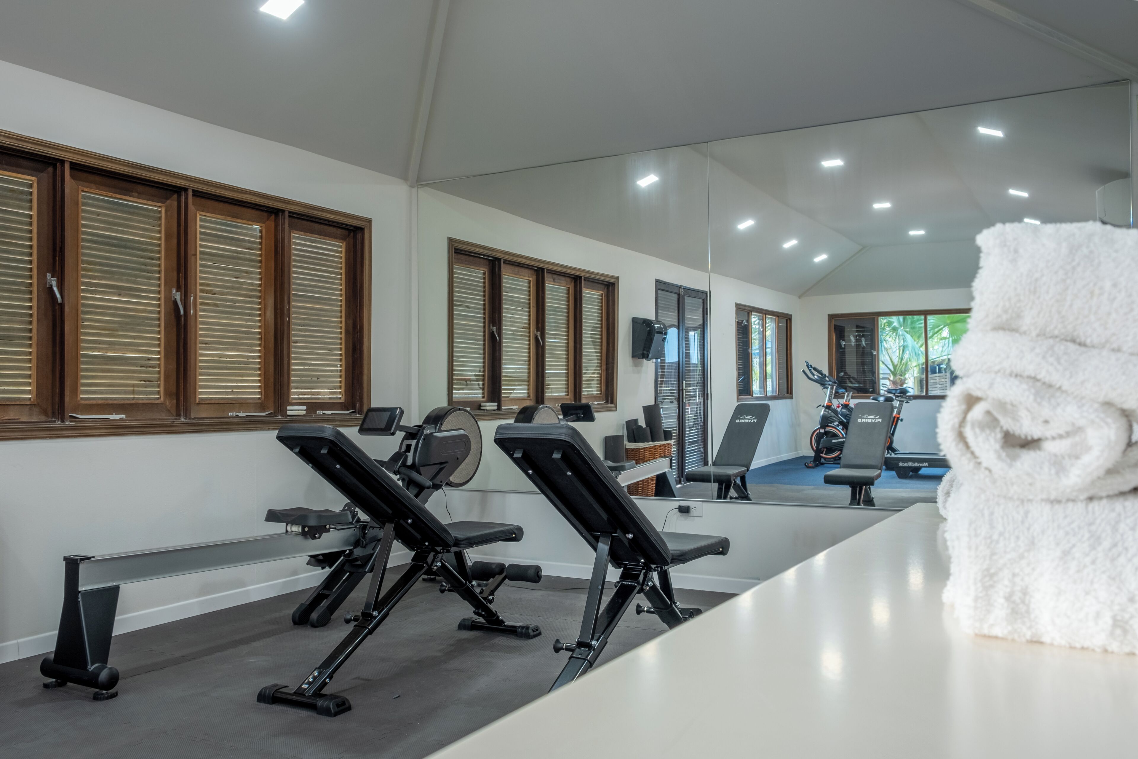 A gym with exercise equipment, a white towel, and large windows with blinds.