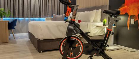 Una habitación de hotel moderna con una bicicleta estática, una cama, un escritorio y una planta en maceta.