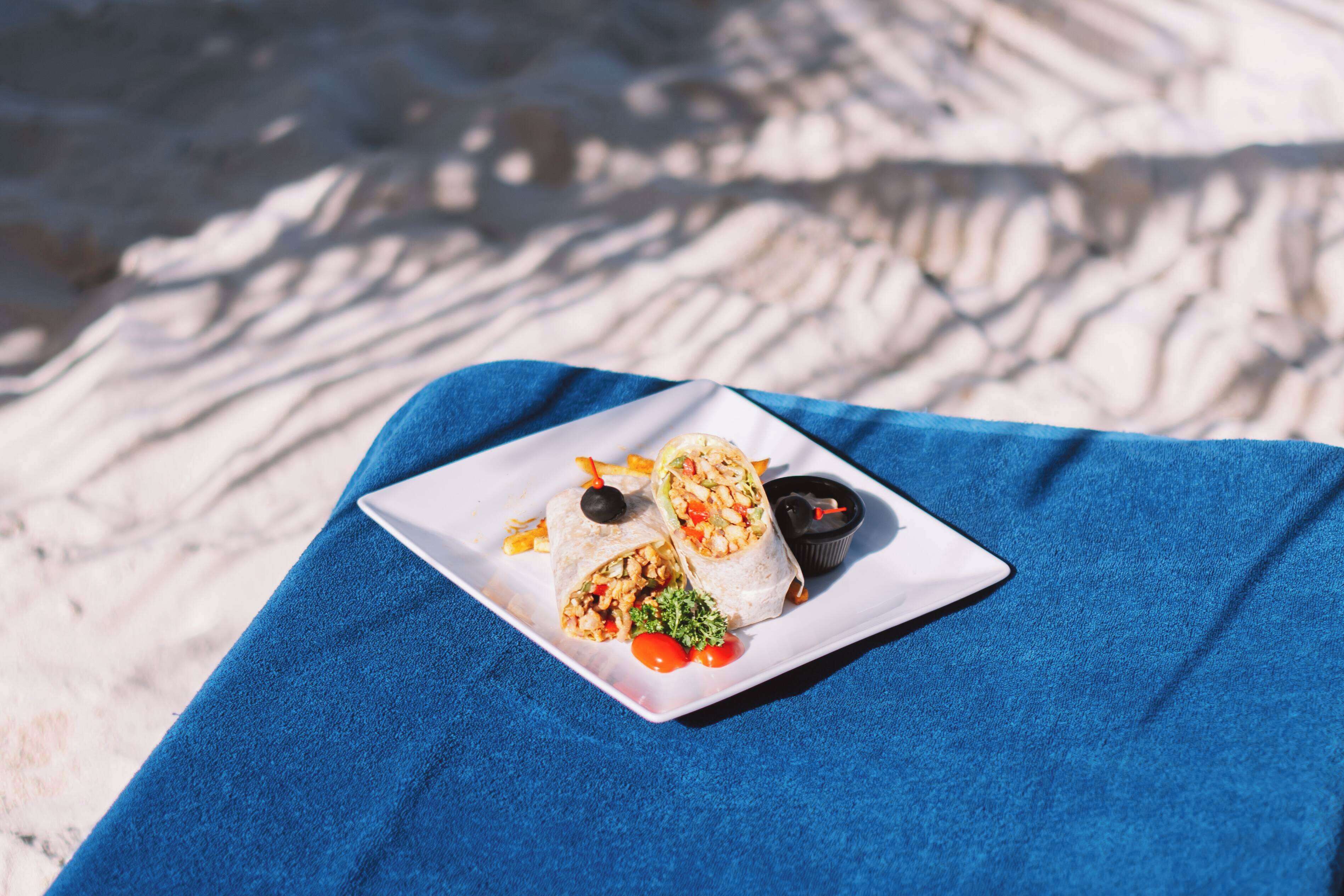 Un plato blanco con dos wraps, un recipiente negro para salsa y un tazón pequeño de salsa sobre una toalla azul.