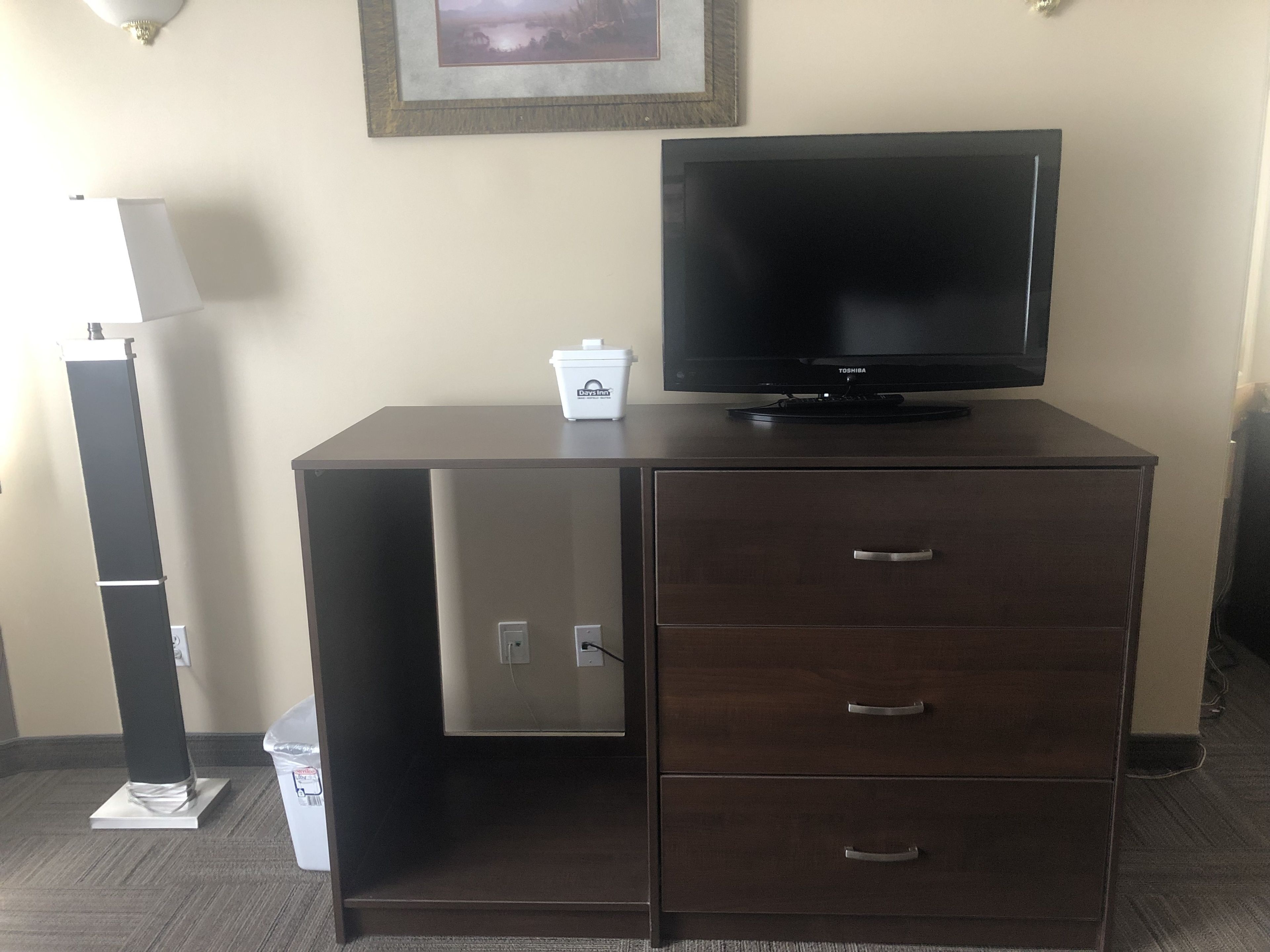 Een donker houten kast met een flatscreen televisie erop, een klein wit doosje met de tekst 'Days Inn', en een afvalbak links.