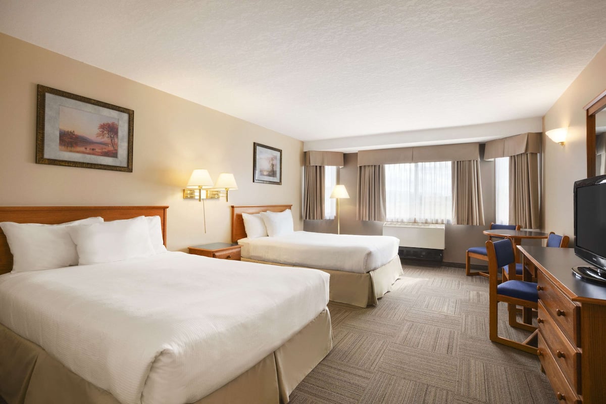 A hotel room with two beds, a desk with a chair, a television, and two wall-mounted lamps.