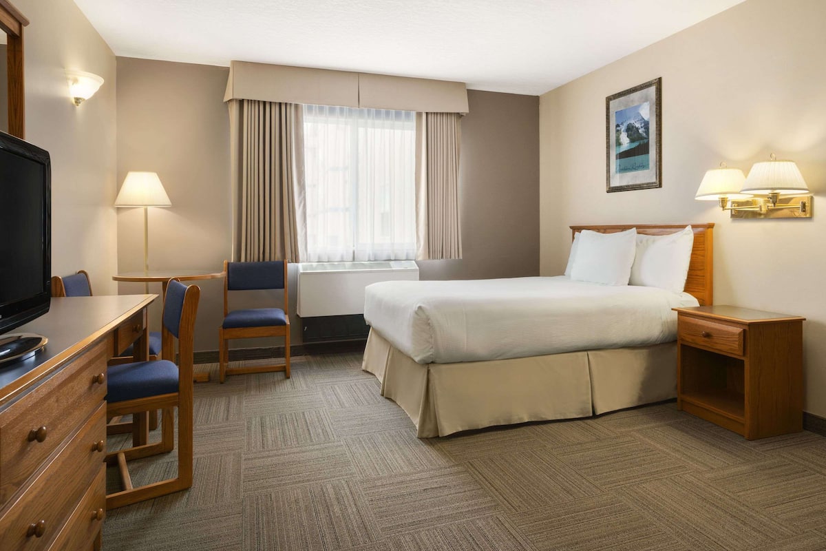 A hotel room with a bed, a desk with a chair, a television, a lamp, and a picture on the wall.
