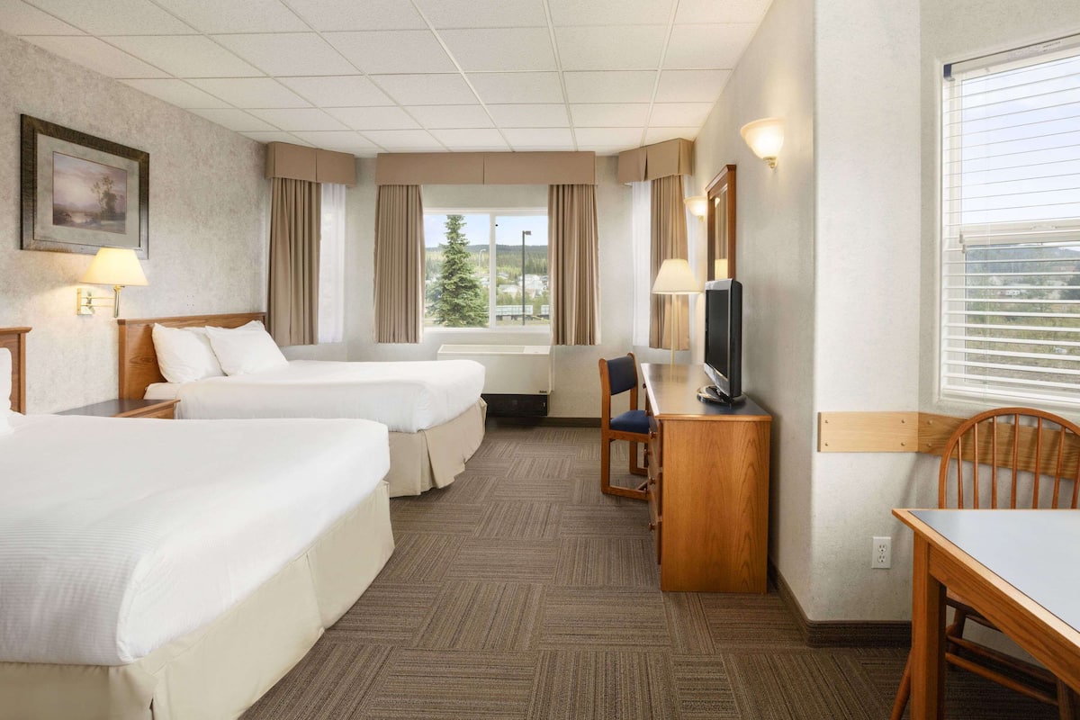 A hotel room with two beds, a desk, a chair, a television, and a window with curtains.