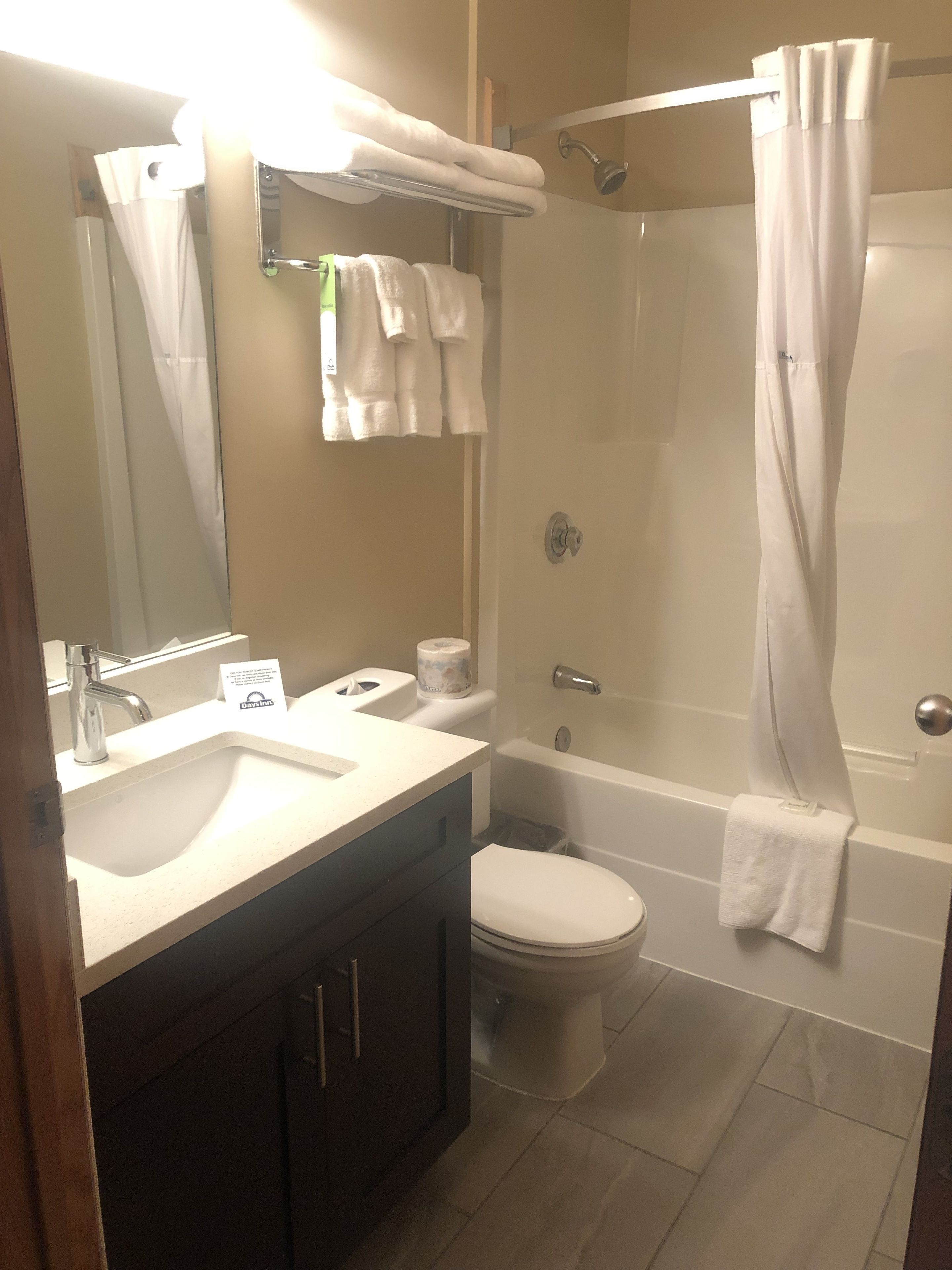 Un baño con lavamanos, inodoro y bañera. Hay toallas colgadas en un perchero y una cortina de ducha.