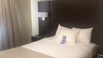 Habitación de hotel con una cama grande, una mesita de noche, una lámpara de pared y una ventana con cortinas.