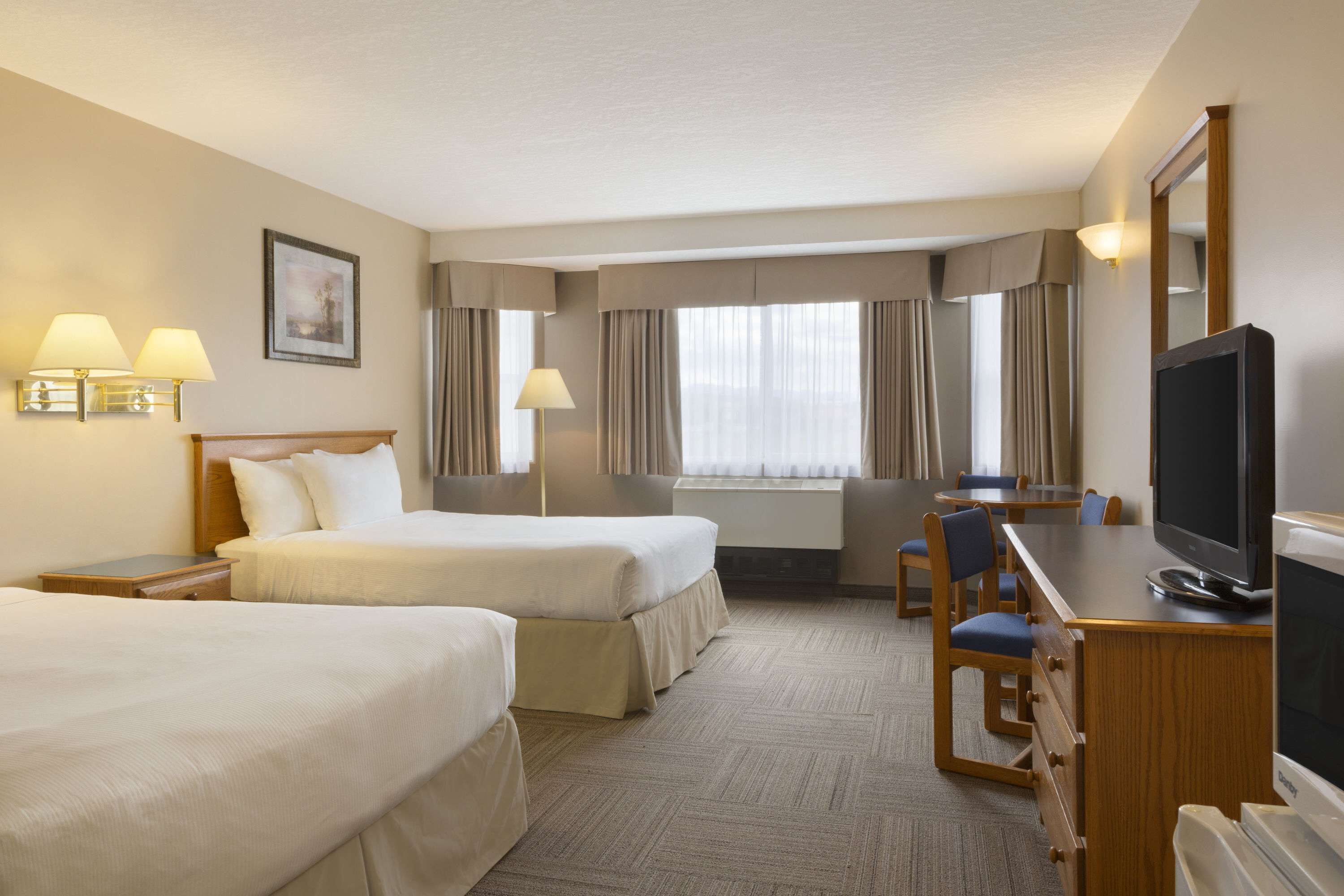 A hotel room with two beds, a desk with a television, and a dining area.