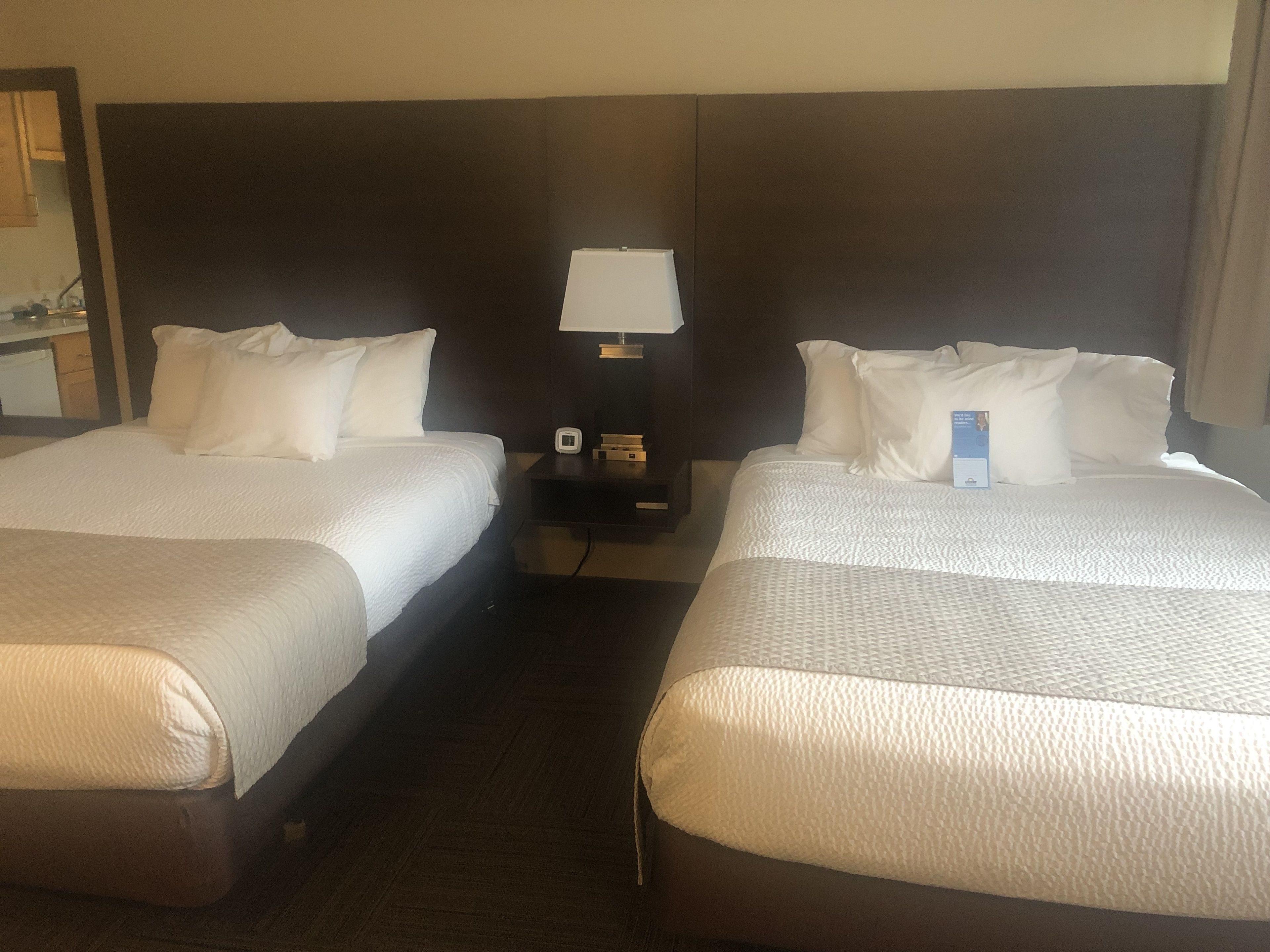 Ein Hotelzimmer mit zwei Betten, einem Nachttisch mit Lampe und einem kleinen Tisch mit Uhr.