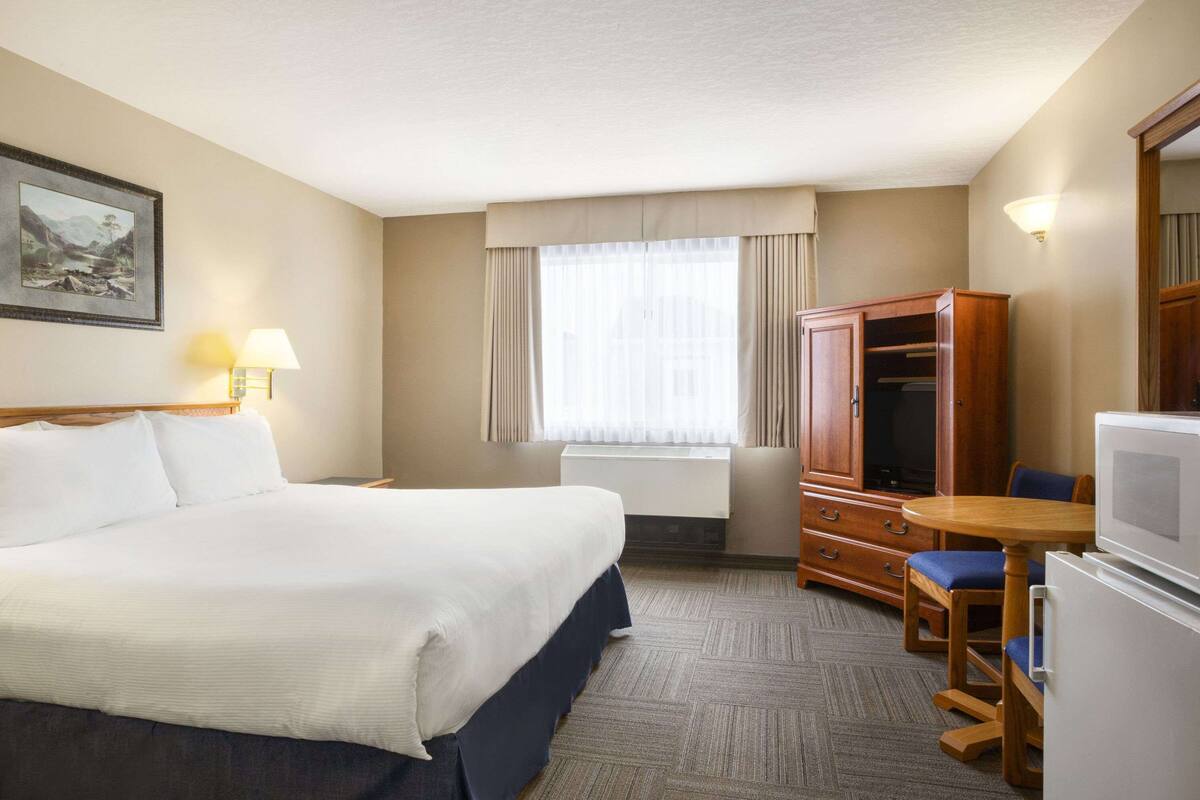A hotel room with a large bed, a wooden wardrobe, a desk with a chair, and a television.