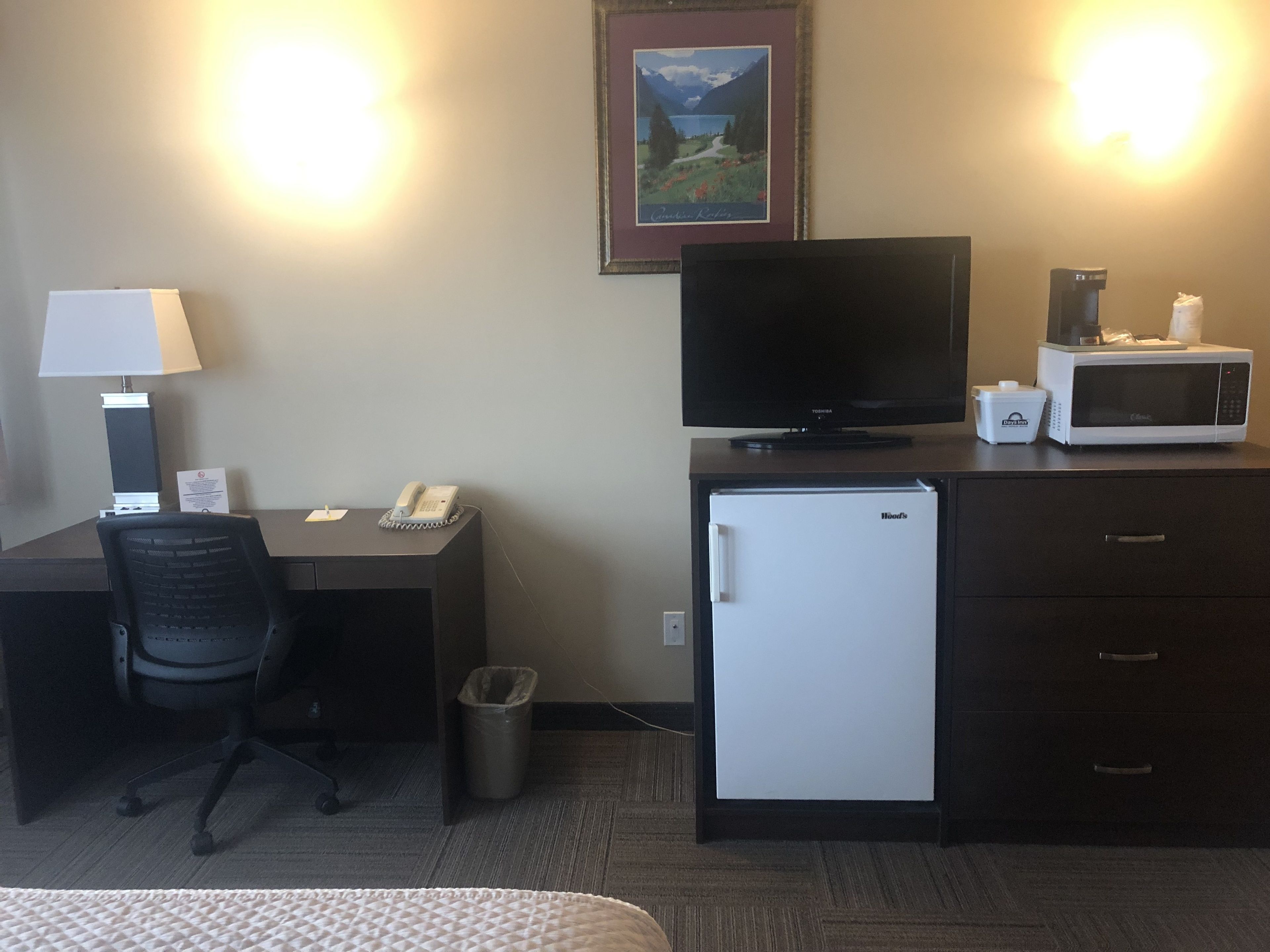 Une chambre d’hôtel équipée d’un bureau, d’une chaise, d’une télévision, d’un four à micro-ondes et d’un petit réfrigérateur.