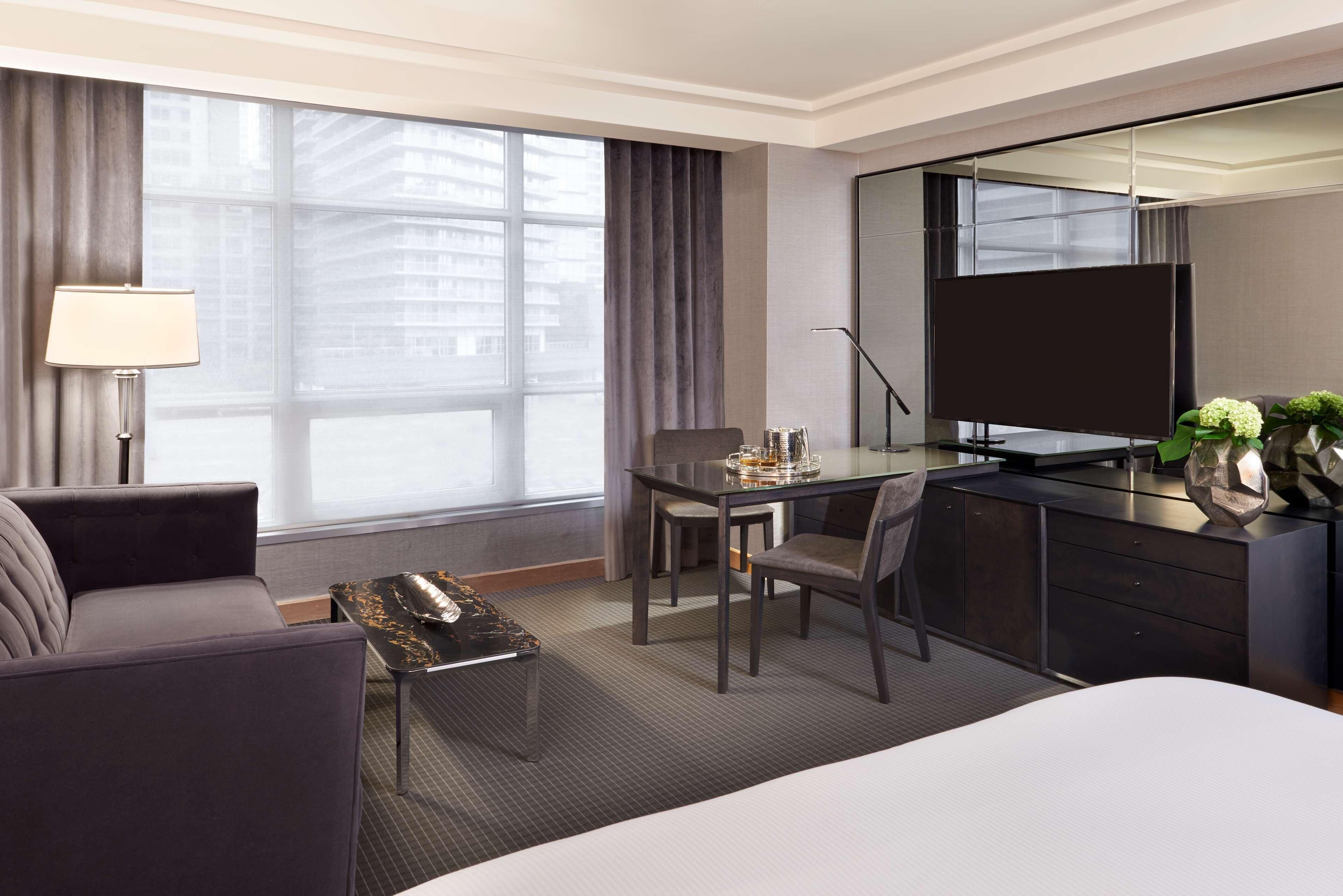 A hotel room with a bed, a desk with a chair, a TV, a lamp, and a window with curtains.