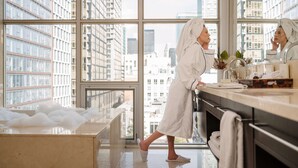 A modern bathroom with a large window, a bathtub filled with bubbles, and a mirror reflecting the cityscape. - Soho Hotel Toronto (Toronto)