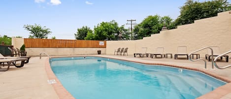 A swimming pool with lounge chairs and a wooden fence in the background.