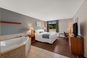 A hotel room with a large bathtub, a bed with a blue and white patterned blanket, a desk with a television, and a window with curtains. - SureStay Plus Hotel by Best Western Berkeley Springs (Berkeley Springs)