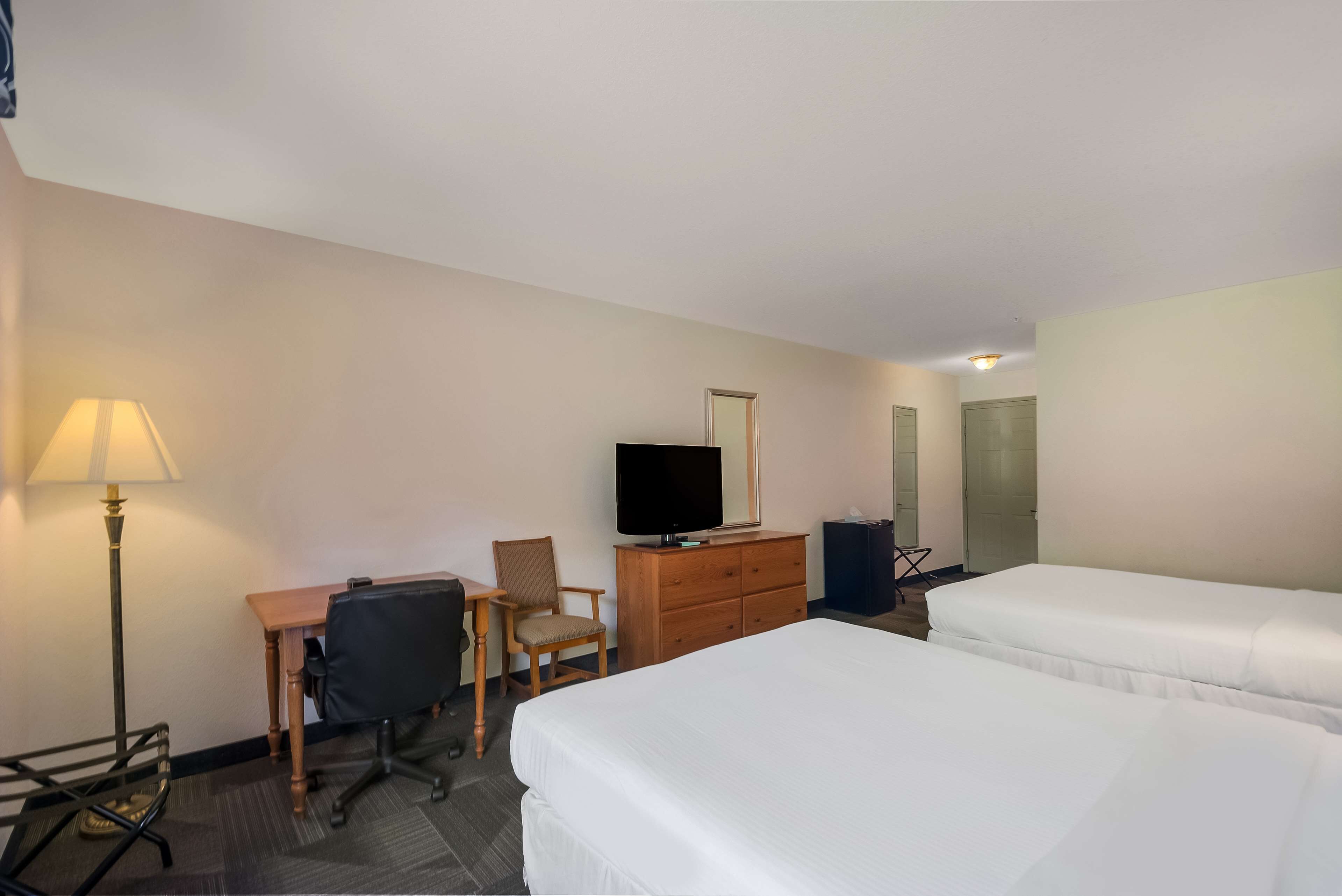 Een hotelkamer met een bureau, stoel, televisie, dressoir en twee bedden.
