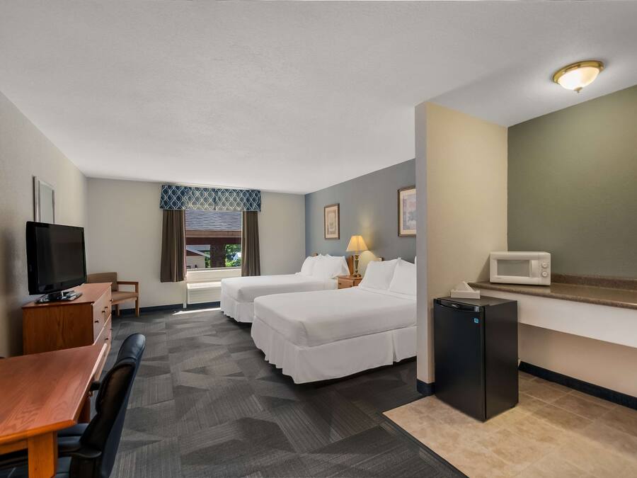 Habitación de hotel con dos camas, un escritorio, televisor, microondas y refrigerador pequeño.