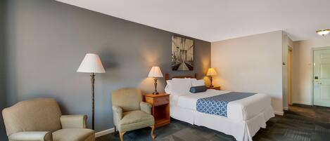 A hotel room with a bed, two chairs, a nightstand, and a floor lamp.