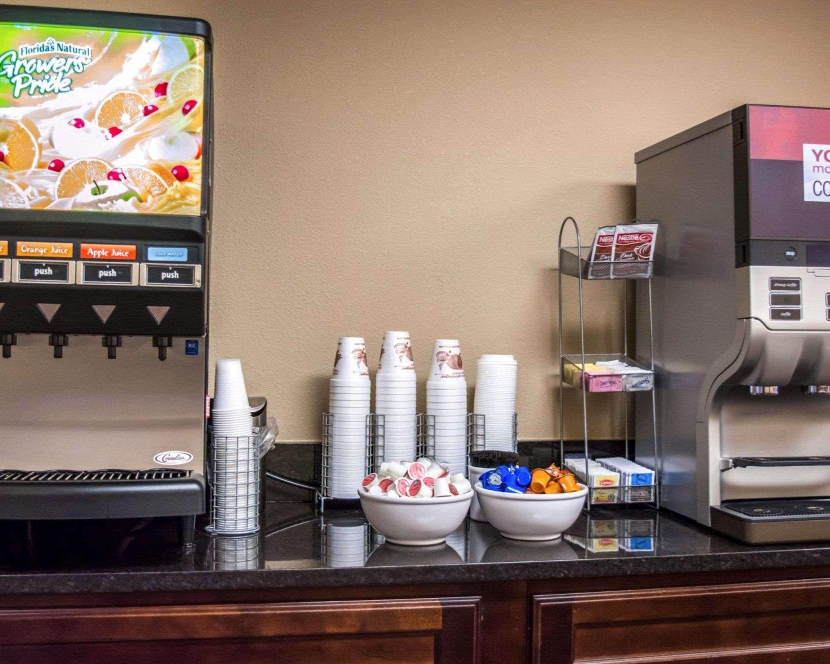 Een drankstation met een keuze aan vruchtensappen en een koffieapparaat, plus een schaal met snacks en een stapel wegwerpbekers.