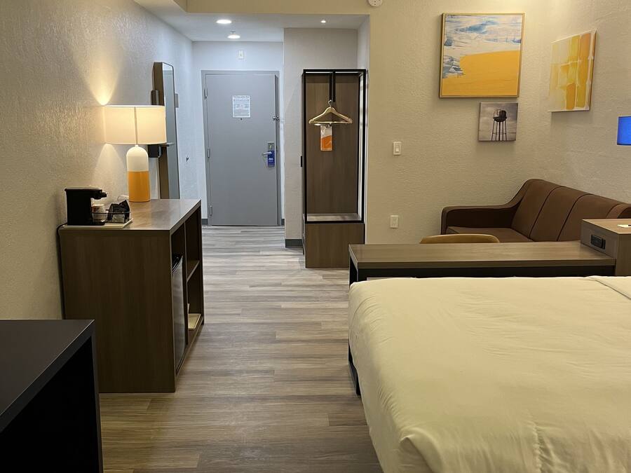 Une chambre d’hôtel comprenant un lit, un bureau, une commode, un porte-manteau et une porte donnant sur une autre pièce.