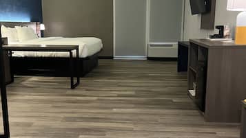 A hotel room with a bed, bedside table, TV, and a desk with a lamp.