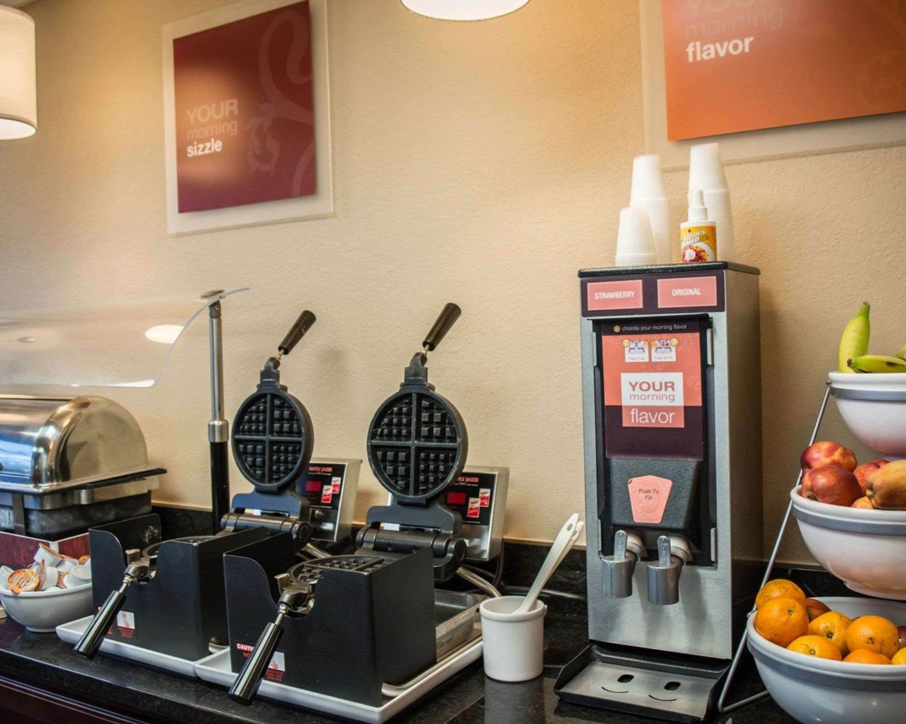A breakfast station with waffle makers, a coffee machine, and a fruit bowl.