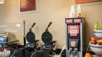A breakfast station with waffle makers, a coffee machine, and a fruit bowl.