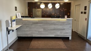 A reception desk with a modern design, featuring a wooden panel backdrop and three pendant lights. - Comfort Suites Clearwater - Dunedin (Clearwater)