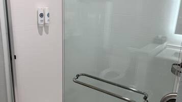 Un box de ducha con paredes de vidrio, una manija de metal y un dispensador de jabón en la pared.