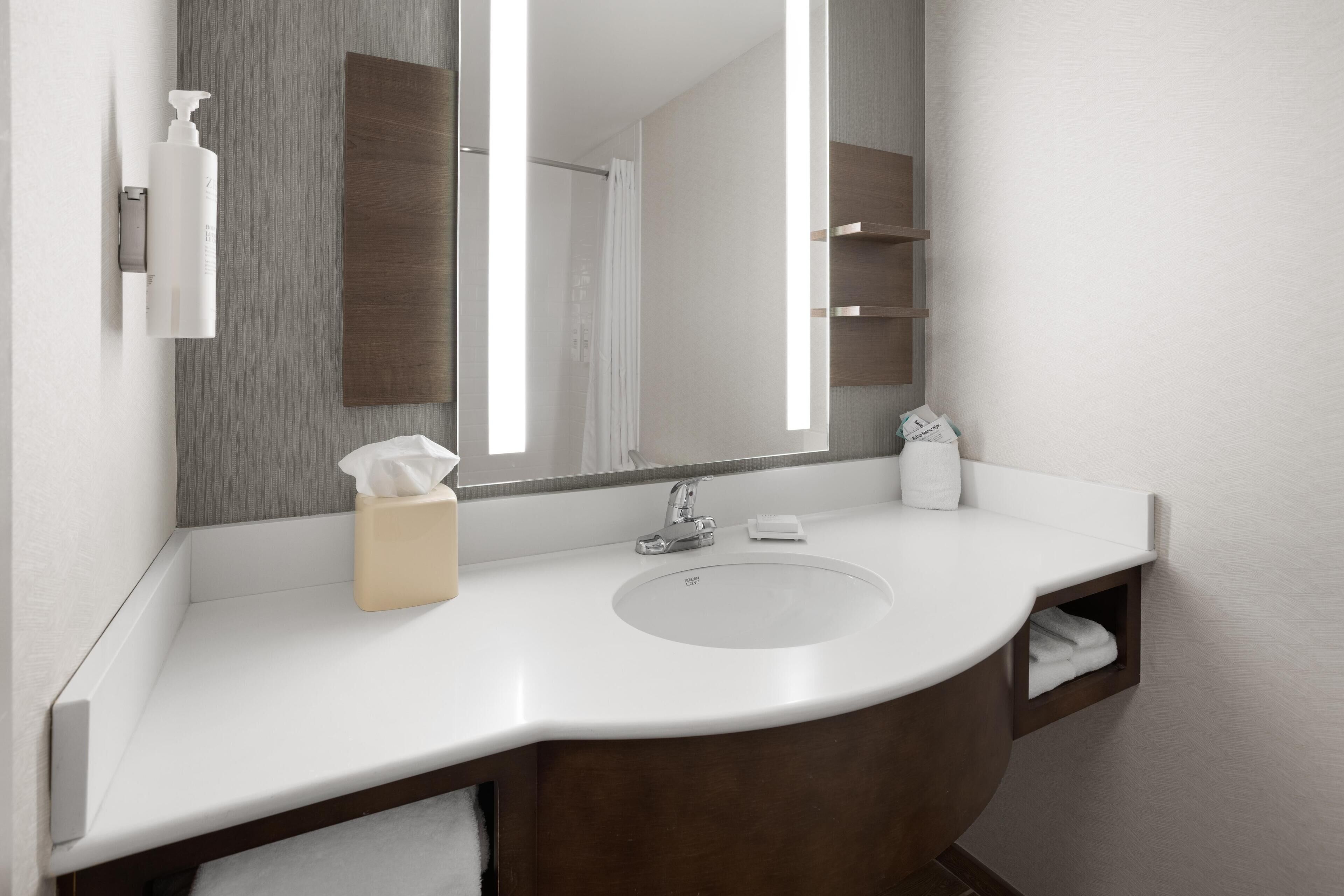 A modern bathroom with a white sink, a large mirror, and a wooden vanity.