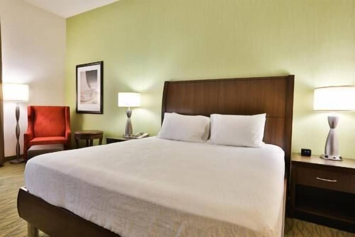 Hotellihuone, jossa on suuri sänky, tuoli, työpöytä ja lamppu.