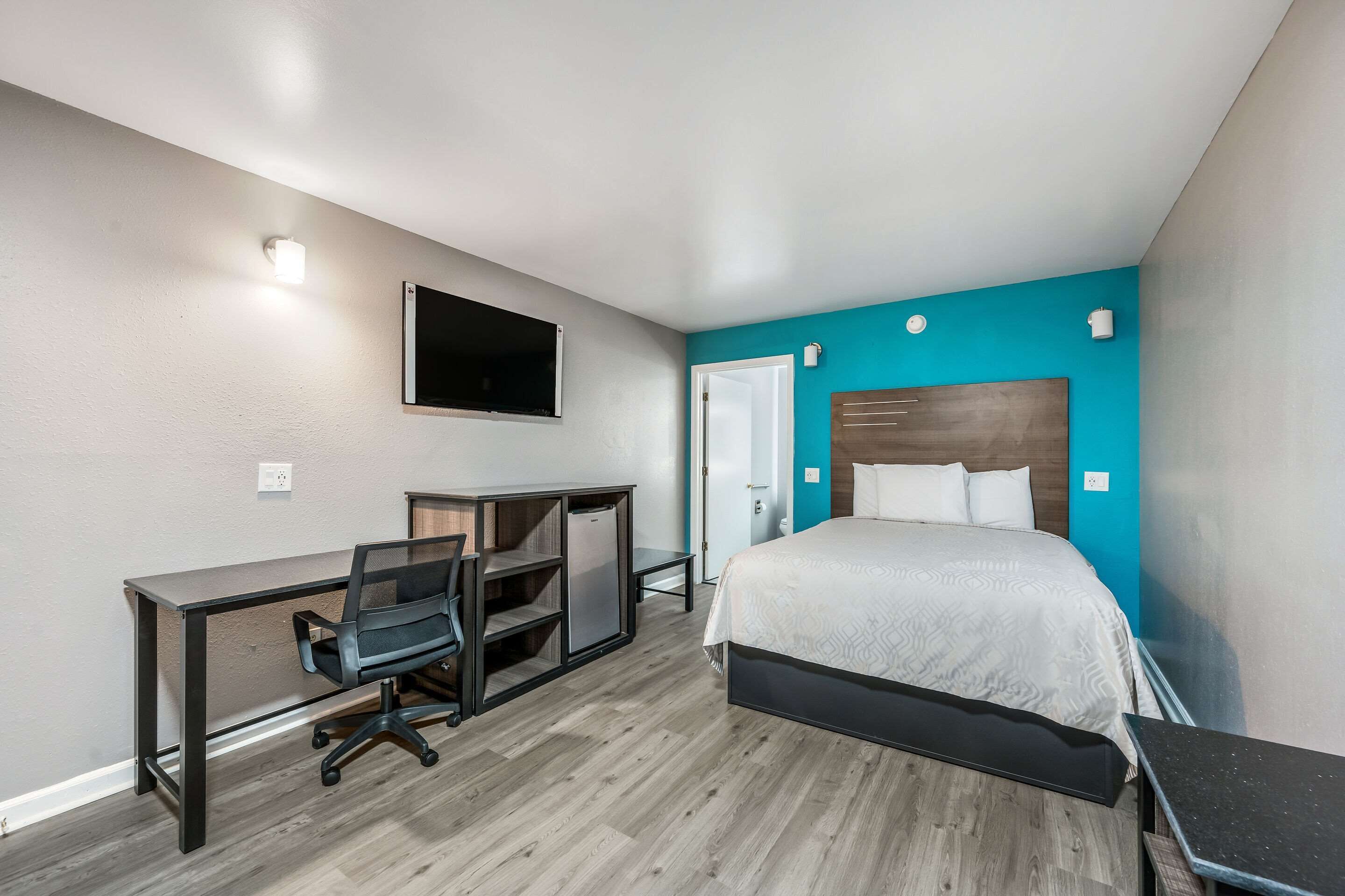Une chambre à coucher avec un lit, un bureau, une chaise et un téléviseur fixé au mur.