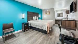 A modern hotel room with a teal accent wall, a bed with a headboard, a desk with a chair, a small table, and a built-in TV. - Econo Lodge Russellville (Russellville)