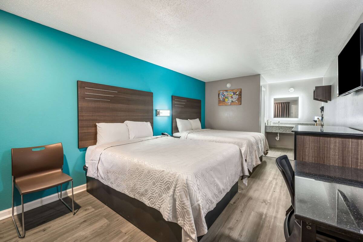 A hotel room with two beds, a desk, a chair, and a bathroom visible in the background.